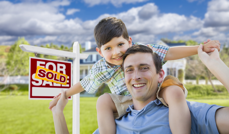 Father  and son piggyback in front of San Francisco house with  sold sign, celebrating their home just got sold.