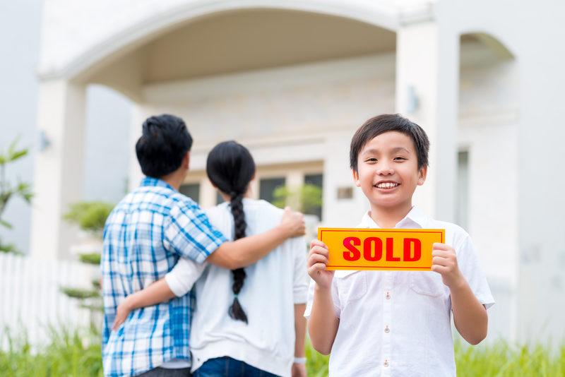 Asian boy holding sold sign in front of Georgia home