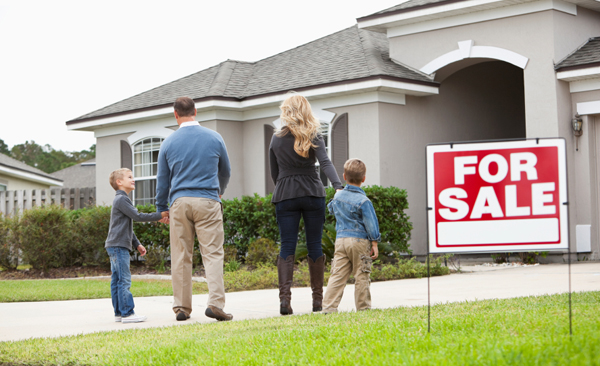 Family with two boys (4 and 6 years) walking toward house with FOR SALE sign in front yard.