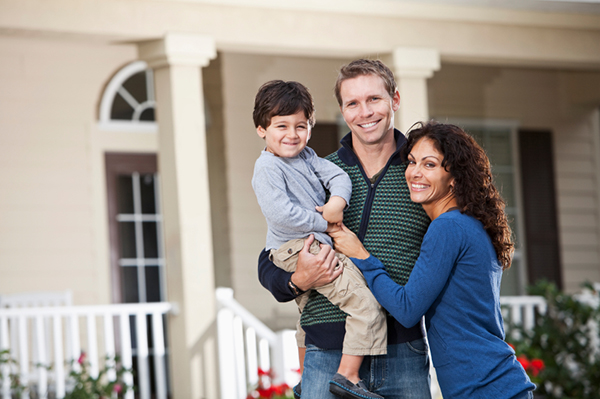 Family with little boy standing in front yard of home