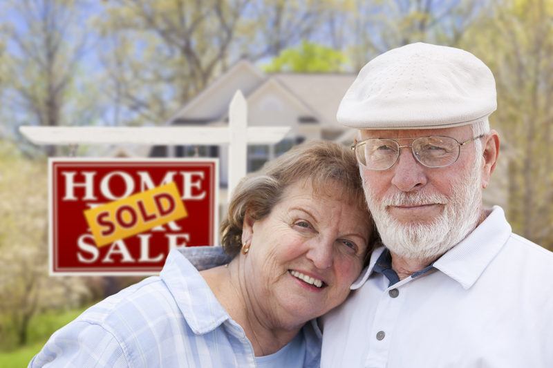 Senior Alabama Couple in Front of Sold Real Estate Sign and House
