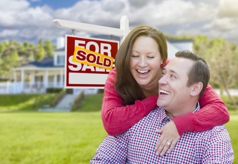 Laughing Couple In Front of Sold For Sale Sign and House in Arizona