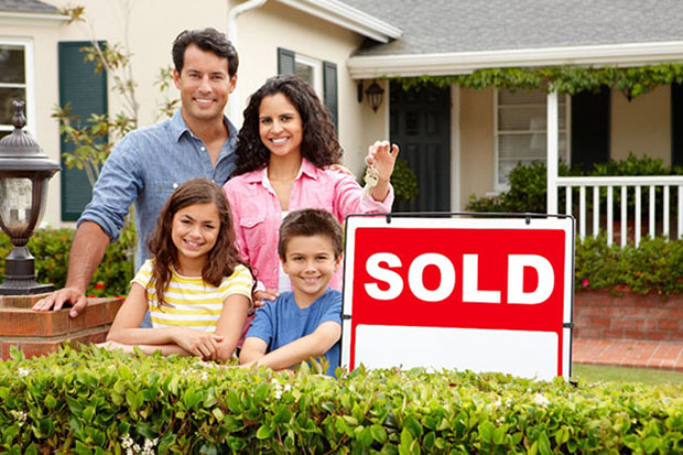 Hispanic looking family standing in front of their home while holding house keys next to a SOLD sign.