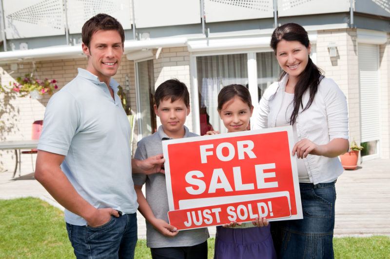 Family with a sale sign outside their new home